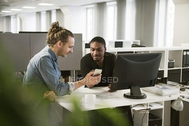 Работники используют смартфон, сидя за рабочим столом в офисе — стоковое фото