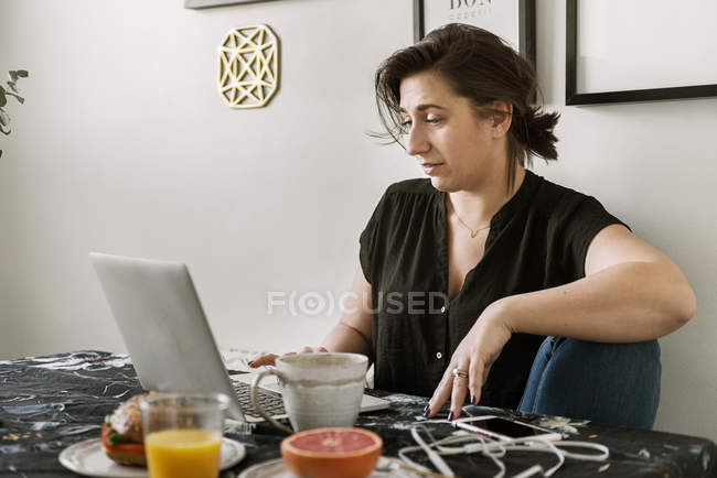 Mujer joven usando el ordenador portátil durante el desayuno - foto de stock