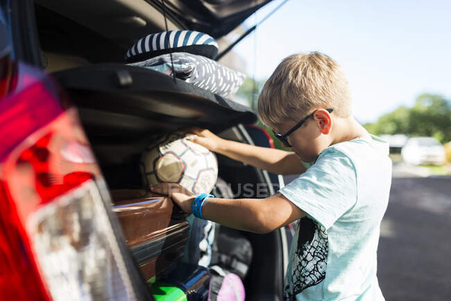 Мальчик берет футбол из багажника машины — стоковое фото