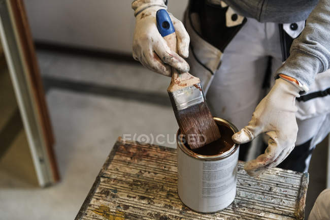 Hands of painter dipping paintbrush into paint can — Stock Photo