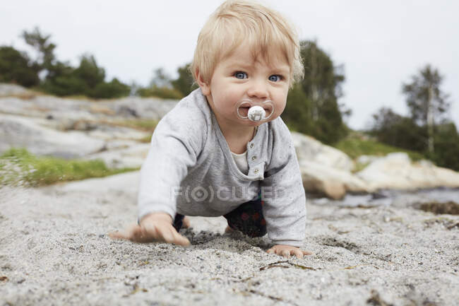 Menina de bebê rastejando e olhando para a câmera na praia — Fotografia de Stock