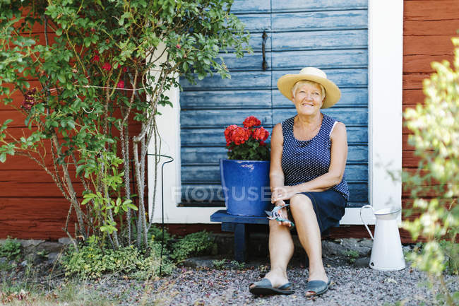 Senior mulher sentada por vaso de flores na frente da porta — Fotografia de Stock