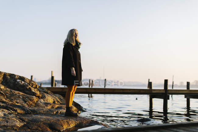 Жінка стоїть на каменях біля моря під час заходу сонця — стокове фото