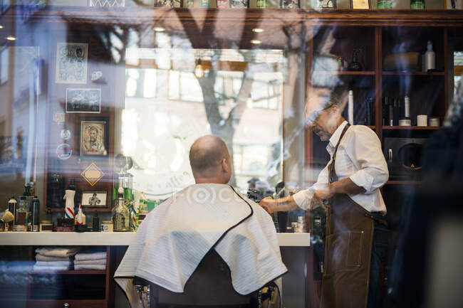 Barber talking to customer in barbershop window — Stock Photo