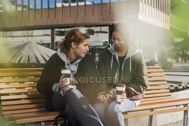 Les adolescentes utilisant un téléphone intelligent sur le banc — Photo de stock