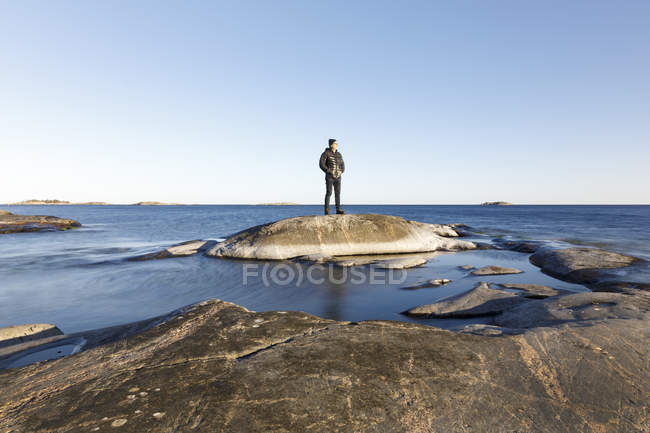 Homme debout sur un rocher au bord de la mer, objectif sélectif — Photo de stock