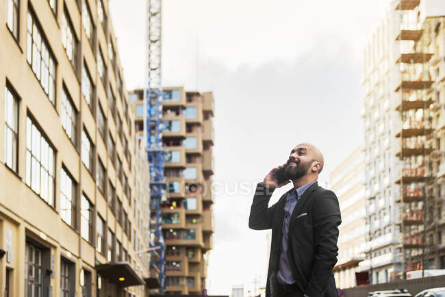 Низький кут зору усміхненого бородатого бізнесмена, що розмовляє по смартфонах у місті — стокове фото