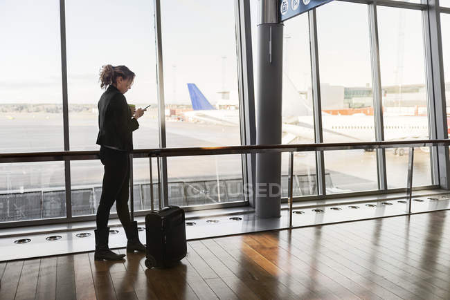 Жінка з валізою і смартфоном в аеропорту — стокове фото