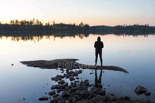 Uomo in piedi sulla roccia nel lago al tramonto — Foto stock