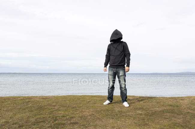 Homem de camisola com capuz em pé perto do lago — Fotografia de Stock