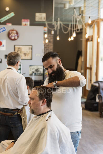 Barbers cutting customers hair in barbershop — Stock Photo