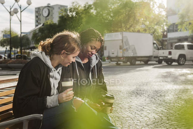 Adolescentes usando telefone inteligente no banco — Fotografia de Stock