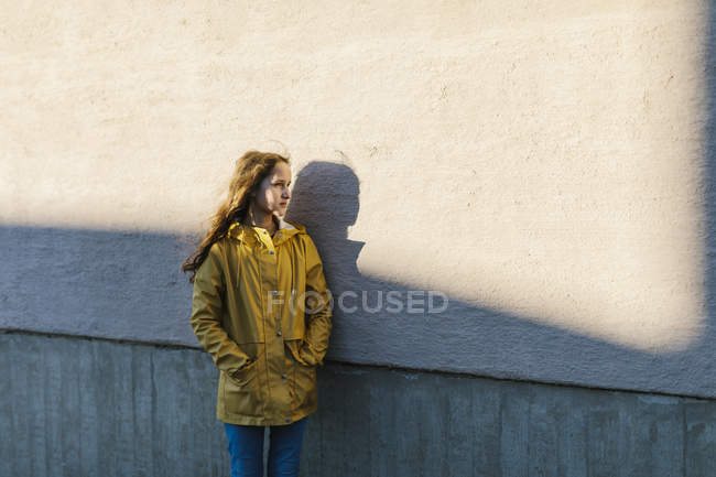 Chica vistiendo impermeable amarillo por pared gris en sombra - foto de stock