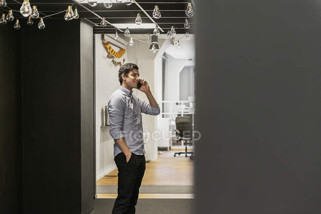 Junger Mann steht mit der Hand in der Tasche und telefoniert im Büro — Stockfoto