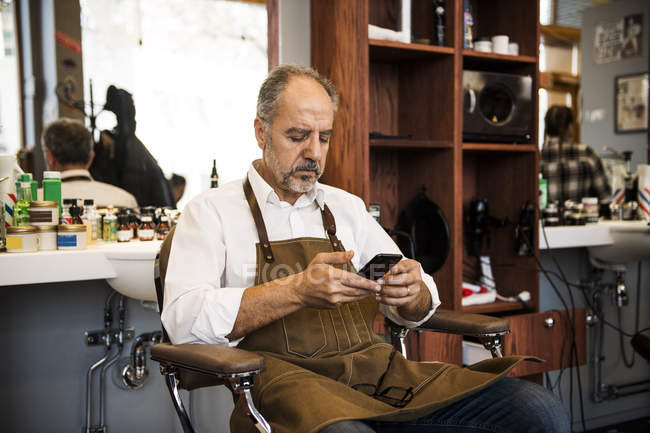 Barber using smartphone in barbershop, selective focus — Stock Photo