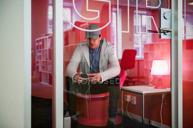 Молодой человек сидит и пользуется смартфоном в офисе — стоковое фото