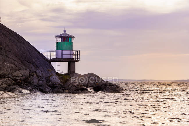 Phare sur les rochers par la mer au coucher du soleil dans la baie de Kanholm, Suède — Photo de stock