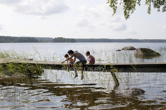 Homem sentado com crianças no cais do lago — Fotografia de Stock