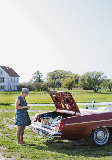 Femme mûre debout à côté de voiture vintage au champ — Photo de stock