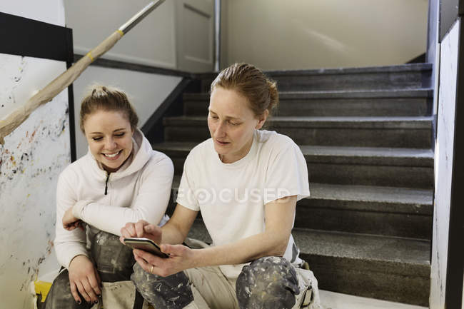 Pintores usando teléfono inteligente en la escalera del apartamento - foto de stock