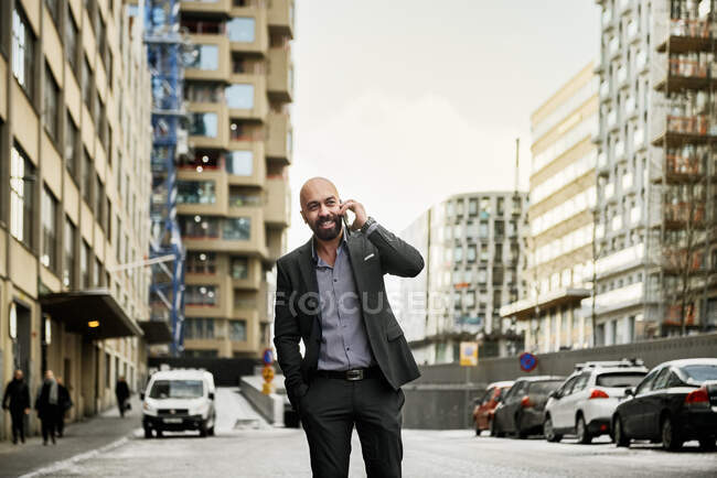 Усміхнений бородатий бізнесмен розмовляє по смартфону в місті — стокове фото