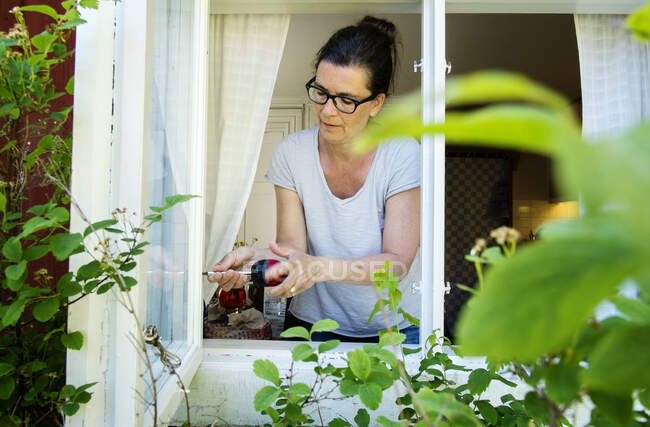 Взрослая женщина в очках капает из окна — стоковое фото