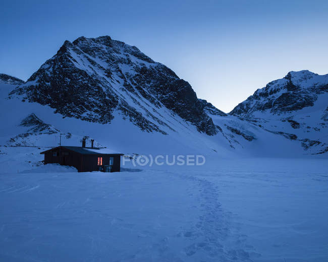 Cabin in snow by mountain at sunset — Stock Photo