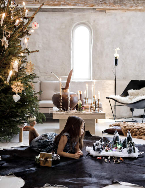 Girl lying by nativity scene and Christmas tree in living room — Stock Photo