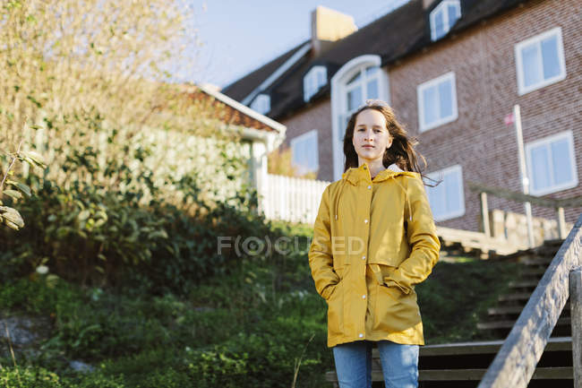 Menina vestindo capa de chuva amarela na escada por casa — Fotografia de Stock