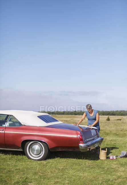 Mature woman traveling on vintage car, looking on map at field — Stock Photo