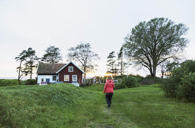 Woman walking in field by house — Stock Photo