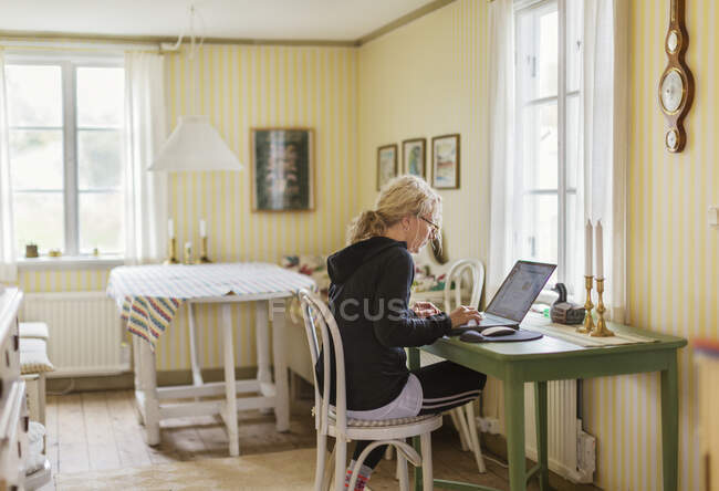 Середня доросла жінка по телефону за ноутбуком — стокове фото