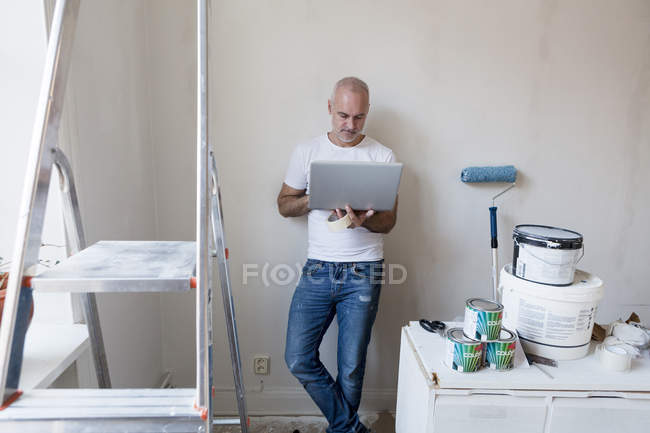 Mid adult man looking at laptop during apartment renovation — Stock Photo