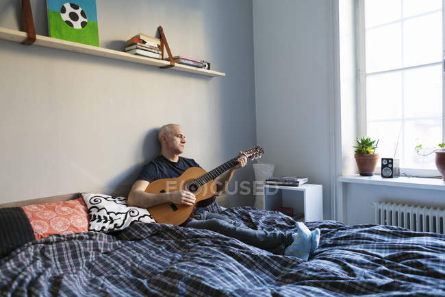 Homem sênior tocando guitarra na cama — Fotografia de Stock