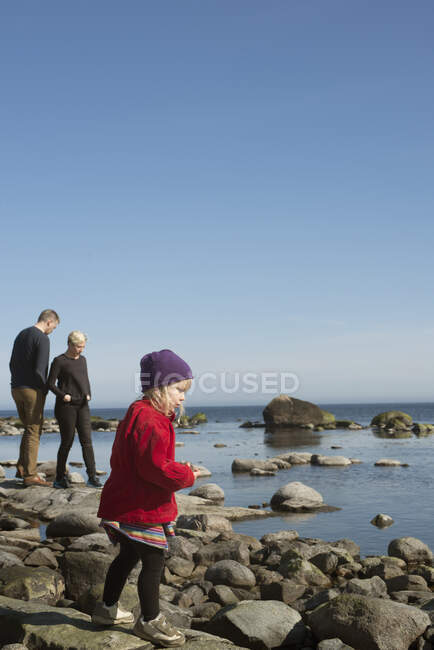 Parents with daughter standing on rocks near sea — Stock Photo