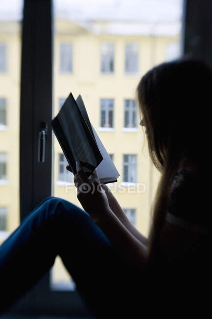 Teenagermädchen liest Buch im Sitzen am Fenster, Seitenansicht — Stockfoto