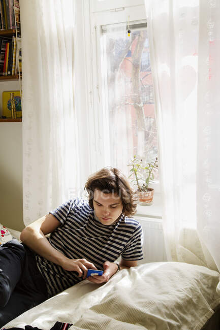 Junger Mann schaut im Schlafzimmer auf Handy — Stockfoto