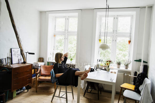 Mujer joven sentada con los pies en un apartamento - foto de stock