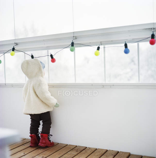 Vue arrière de l'enfant portant des vêtements chauds et regardant par la fenêtre — Photo de stock