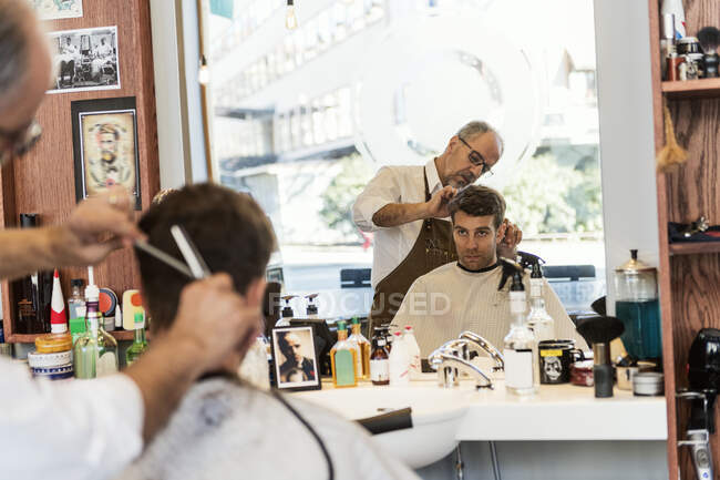 Barber cutting young man hair, selective focus — Stock Photo