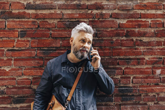 Homem ao lado da parede de tijolo falando no telefone inteligente — Fotografia de Stock