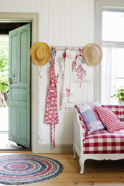 Straw hats and apron hanging on hook between door and sofa — Stock Photo
