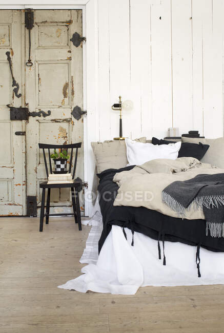 Bed by weathered door on hardwood floor — Stock Photo