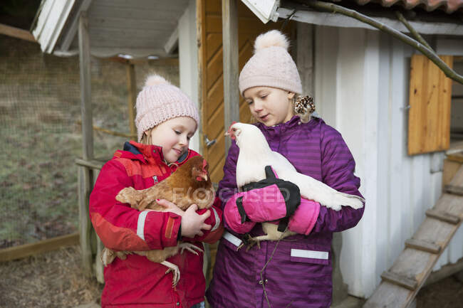 Sisters with warm cloathing holding chickens — Stockfoto