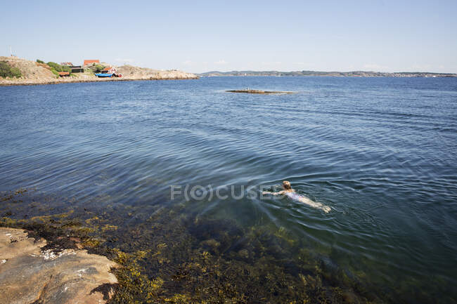 Chica nadando en el mar bajo el cielo despejado - foto de stock