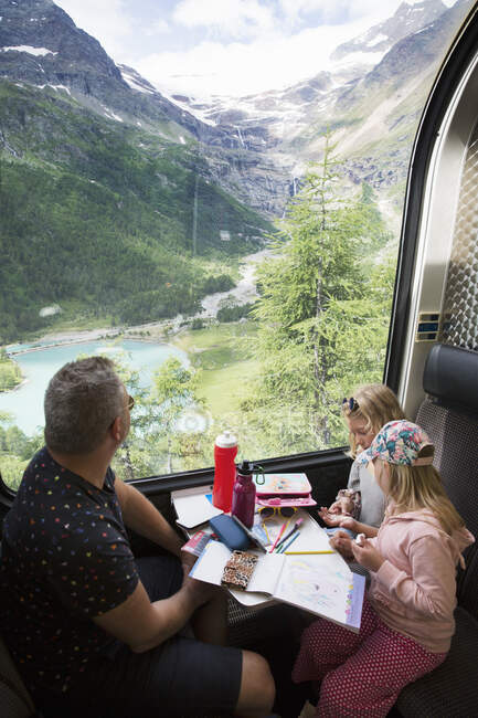 Family sitting on train by mountains - foto de stock