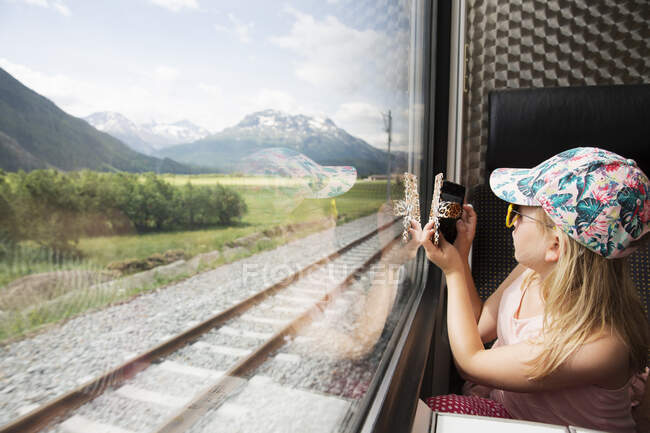 Girl on train taking photograph of mountains on smartphone — Foto stock