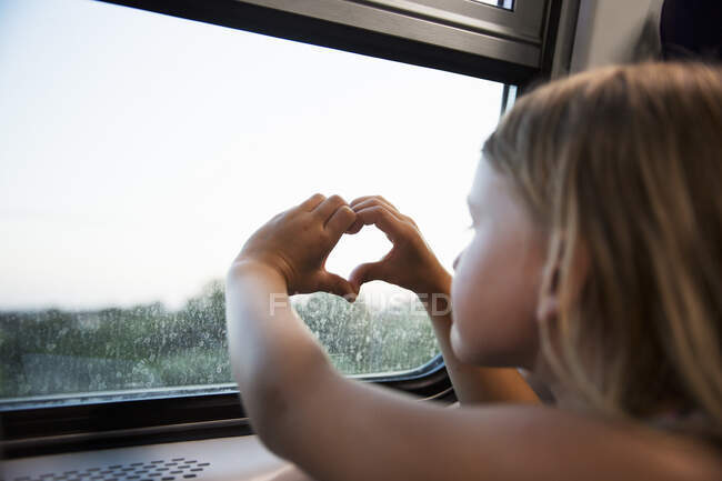 Girl making heart gesture by train window — Stockfoto
