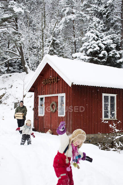 Family walking in snow by cabin — Stockfoto