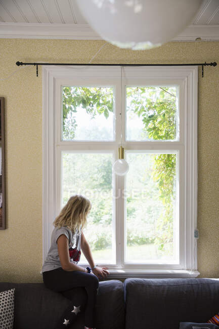 Girl sitting by window looking away — Photo de stock